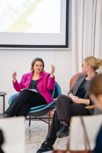 Zbliżenie na na dwie uczestniczki panelu. Jedna z nich ubrana w intensywnie różowy żakiet wypowiada się gestykulując rękami. Druga zwrócona jest twarzą w jej kierunku.